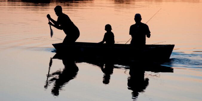 silhouette of three person riding on boat on body of water