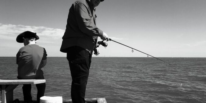 man in black jacket and pants fishing on sea